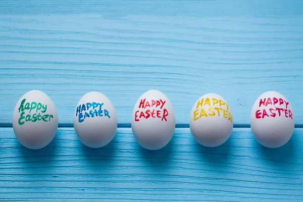 Oeufs de Pâques avec des titres de couleur Joyeuse Pâques écrite par pinceau sont sur le fond en bois de couleur bleue . — Photo