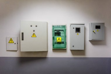 Metal and plastic electric breaker boxes with yellow electrical warning signs of danger  high voltage are installed on the wall in office center clipart