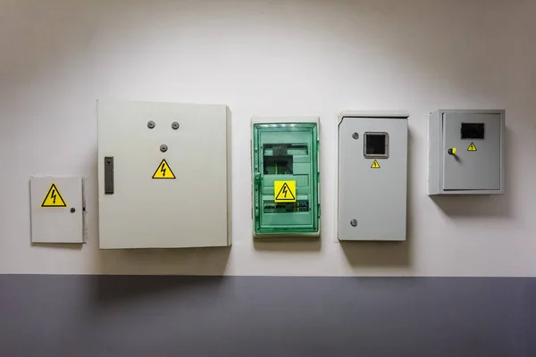 Metal and plastic electric breaker boxes with yellow electrical warning signs of danger  high voltage are installed on the wall in office center — Stock Photo, Image