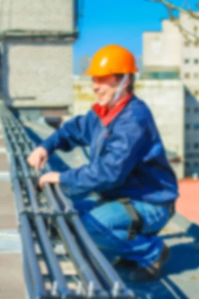 Blurred professional industrial climber in helmet and uniform works at height for instaling communication equipment and antenna.