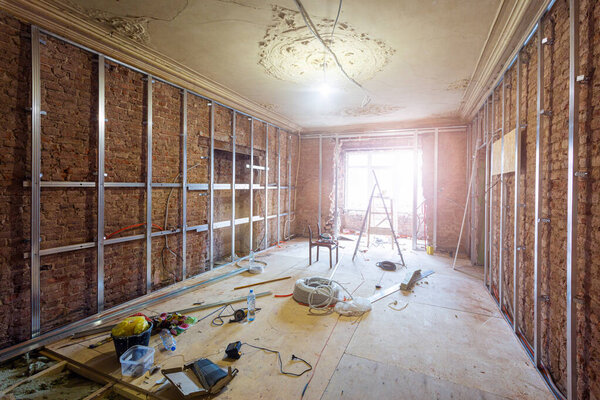 Строительные материалы, инструменты и установленные рамы для гипсокартона для изготовления гипсокартонных стен на кирпичной стене в строящейся квартире, реконструкции, реконструкции, капитального ремонта, удлинения
