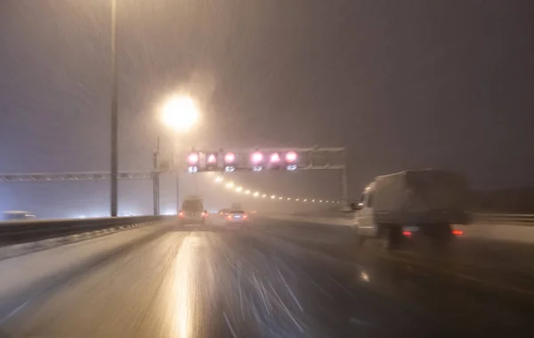 Изображение с размытым движением. Автомобили быстро ездят по зимнему скоростному шоссе или шоссе с дорожным освещением в снежную бурю в сумерках, когда идет снег с дождём. Мбаппе вождения в — стоковое фото
