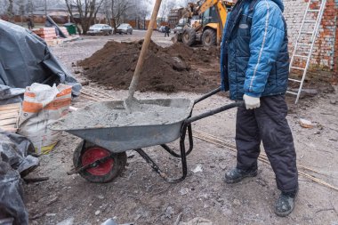 Eldivenleri koruyan işçi inşaat alanındaki betonu yapmak için arabayı kumlu tutuyor. İnşaat, tadilat ve yenileme sırasında inşaat malzemeleri kullanma kavramı