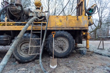 İnşaat alanında büyük tekerlekleri olan eski kamyona hidrolik yeraltı suyu sondaj makinesi yerleştirildi. Yeraltı kuyusu sondajı..