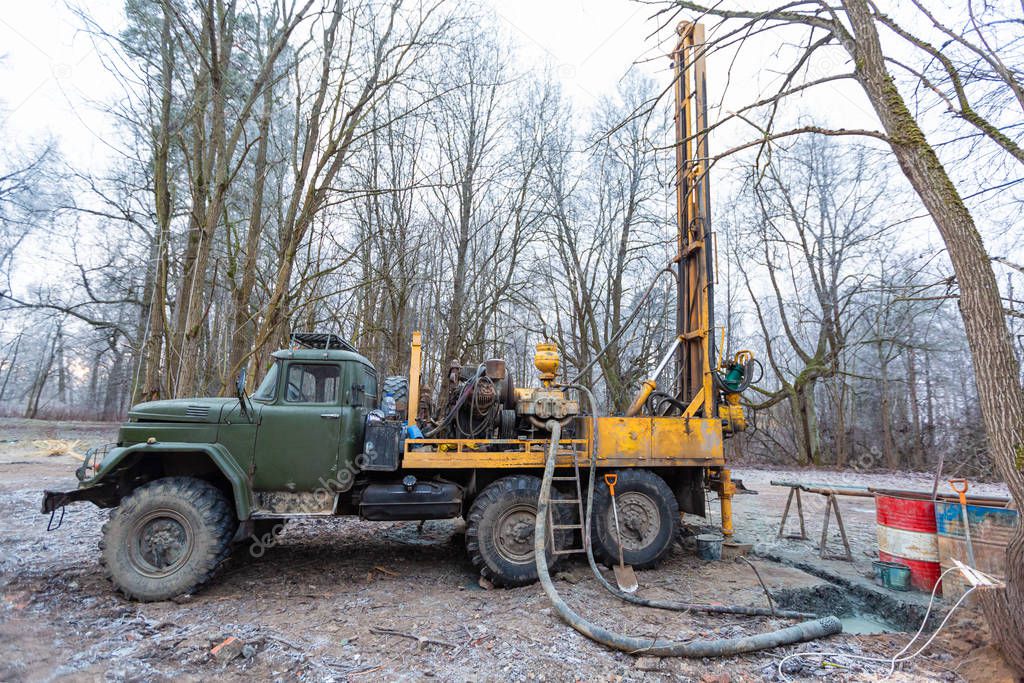 Hydraulic ground water hole drilling machine installed on the old truck with big wheels on the construction site. Groundwater well drilling.