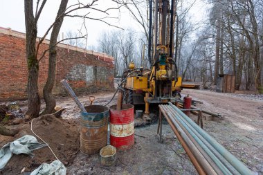 İnşaat alanında büyük tekerlekleri olan eski kamyona hidrolik yeraltı suyu sondaj makinesi yerleştirildi. Yeraltı kuyusu sondajı..