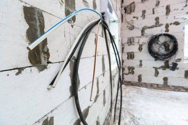 İnşaat alanındaki bina boyunca köpüklü beton bloktan yapılmış duvara sabitlenmiş elektrik kablolarına odaklanmış görüntü. Kablo elektrik yüklemeye hazır