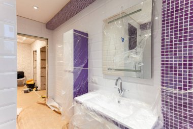Banyo beyaz-mor fayanslarla kaplı, ayna ve hijyen mühendisliği inşaat, tadilat, yenileme, yenileme, uzatma, restorasyon ve yeniden inşa halindeki dairede bulunuyor. Ev geliştirme kavramı