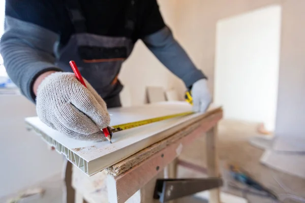 Werknemer is het meten van plastic detail met potlood en tape-line voor het snijden in appartement dat in aanbouw is, verbouwing, renovatie, revisie, uitbreiding, restauratie en wederopbouw — Stockfoto