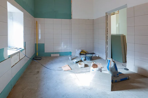 Rum med kaklade väggar med byggmaterial och golv med verktyg i lägenheten som är under uppbyggnad, ombyggnad, renovering, översyn, förlängning, restaurering och återuppbyggnad. Begreppet — Stockfoto