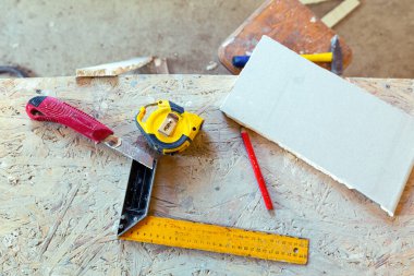 Bazı inşaat malzemeleri - cetvel, inşaat bıçağı, mezura ve kalem, plastik detay inşaat, tadilat, yenileme ve yenileme aşamasındaki dairenin odasındaki beton yonganın üzerinde.