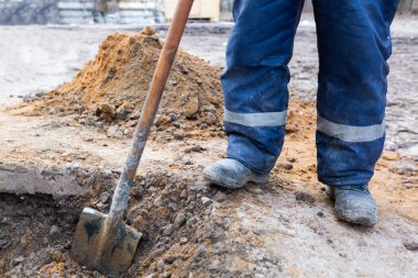 Kirli üniformalı ve kürekli ayakkabılı işçi inşaat alanında bir çukur kazıyor. İnşaat, tadilat, yenileme, yenileme, uzatma, elden geçirme, restorasyon ve