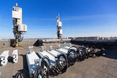 GSM DCS UMTS LTE bantları ve açık hava radyo birimlerinin panel antenleri, temel istasyonun haberleşme ekipmanlarının bir kısmı çatıya kurulmaya hazırlanırken, gökyüzü ve şehir arka plan olarak kullanılıyor. Telekomünikasyon donanımının geliştirilmesi süreci
