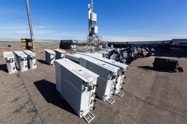 GSM DCS UMTS LTE bantları ve açık hava radyo birimlerinin panel antenleri, temel istasyonun haberleşme ekipmanlarının bir kısmı çatıya kurulmaya hazırlanırken, gökyüzü ve şehir arka plan olarak kullanılıyor. Telekomünikasyon donanımının geliştirilmesi süreci