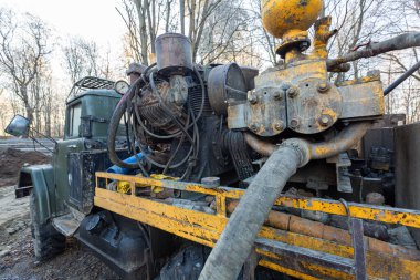 İnşaat alanında büyük tekerlekleri olan eski kamyona hidrolik yeraltı suyu sondaj makinesi yerleştirildi. Yeraltı kuyusu sondajı.