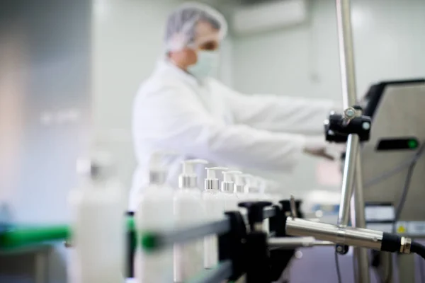 scientist in white coat working in laboratory, bottles with creams on assembly line, production machine of cosmetics