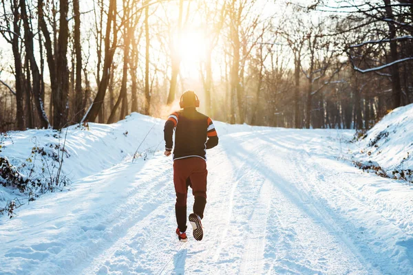 Человек в спортивной одежде бегает в снежном парке — стоковое фото
