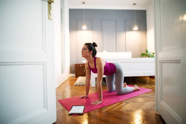 ヨガマットにタブレット 自宅の寝室で折り敷きのヨガ運動をして健康的な美人 — ストック写真
