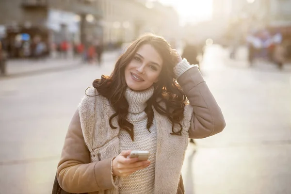 在城市街道使用智能手机的冬天外套的愉快的美丽的妇女 — 图库照片