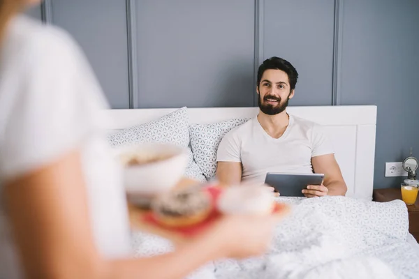 自宅で彼氏にベッドで朝食をもたらす慎重なロマンチックな若い女性 — ストック写真