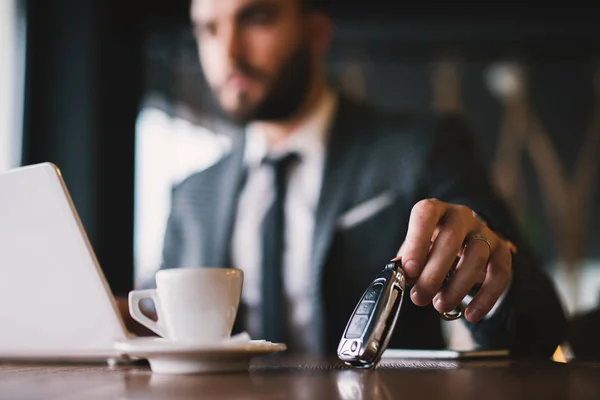 successful young businessman in suit working with laptop at cafe, car keys on foreground