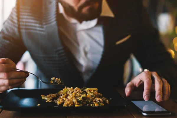 ハンサムな実業家がレストランで食事を食べながら携帯電話をチェック — ストック写真