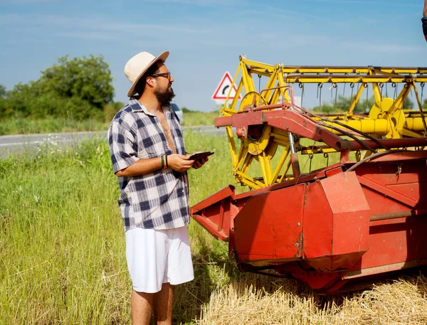 modern farmer with tablet at wheat field near harvester combine