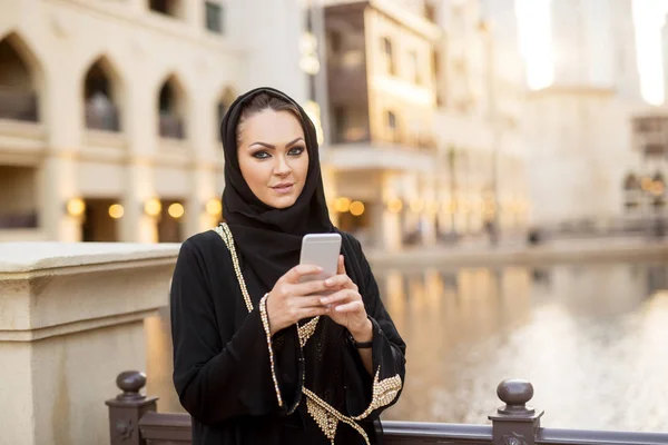 美丽的穆斯林年轻女子在黑色头巾使用智能手机在城市 — 图库照片