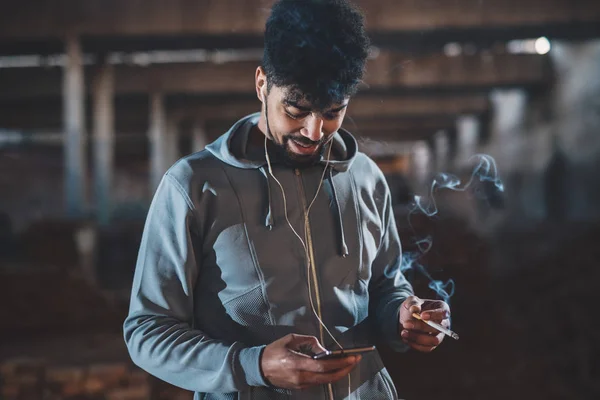 Kulaklık Ile Gece Sokakta Rahatlatıcı Sigara Smartphone Kullanarak Afro Amerikan — Stok fotoğraf