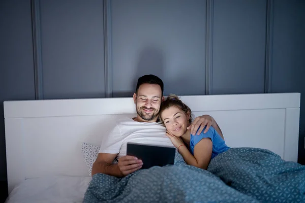 ベッドで横になっていると タブレット 経由で映画を一緒に見て幸せな若者たちの愛のカップル — ストック写真