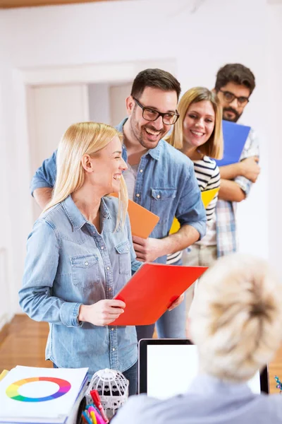 group of smiling young people standing in row with folders before an interview with entrepreneur in office