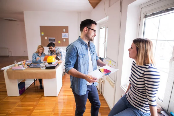 Par Diseñadores Hablando Cerca Ventana Mientras Sus Compañeros Trabajo Trabajan — Foto de Stock