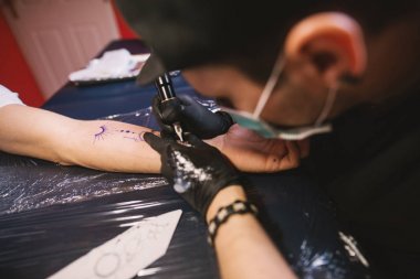 young focused tattoo artist inking arm of customer clipart