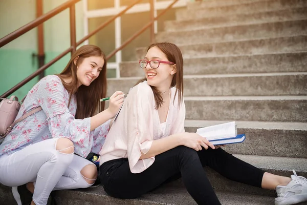两个微笑着漂亮的高中女生一起在楼梯上看书 玩得很开心 — 图库照片