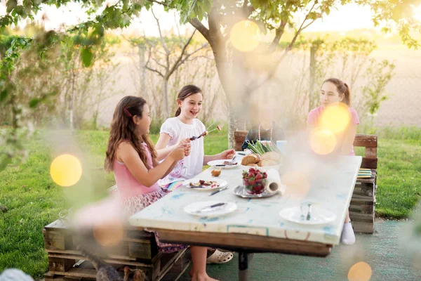 adorable children enjoying picnic sitting at table and eating grilled meat