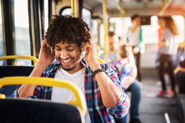 young happy man sitting in a bus seat listening to music through headset