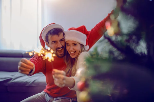 Happy Caucasian Couple Santa Hats Heads Sitting Sofa Holding Sprinklers — Stock Photo, Image