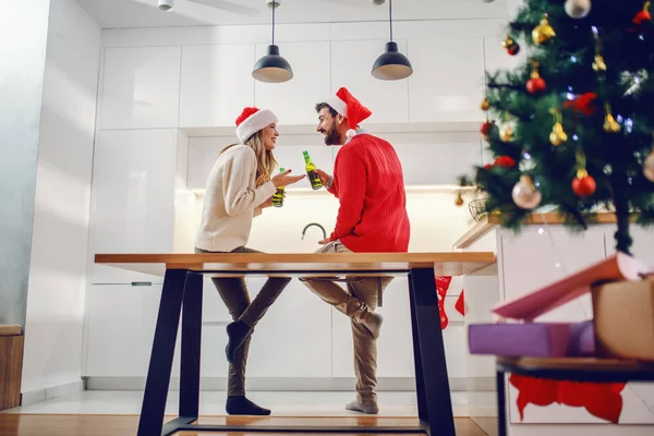 Förtjusande Kaukasiska Par Med Tomte Hattar Huvuden Sitter Köksbänken Hålla — Stockfoto