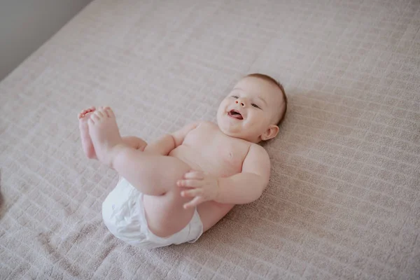 遊び心笑顔かわいいです白人の赤ん坊男の子でおむつベッドの上に横たわる — ストック写真
