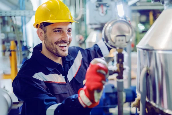 勤劳微笑的蓝领工人穿着防护工作服 站在工厂里拿着灯 带着头盔调节锅炉温度 — 图库照片