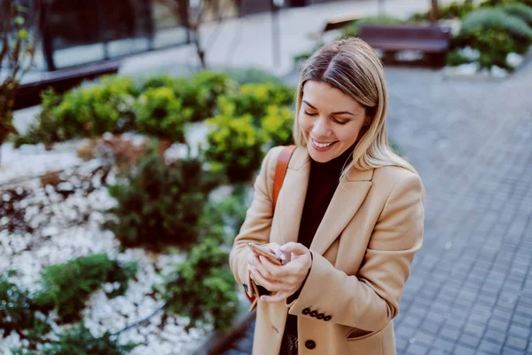 Atraktivní Usmívající Módní Blondýnka Kabátě Stojící Parku Používající Chytrý Telefon — Stock fotografie