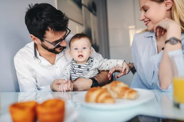 愛らしい男の子とダイニングルームに座っている若い幸せな両親 赤ん坊を抱えてるテーブルの上は朝食 — ストック写真