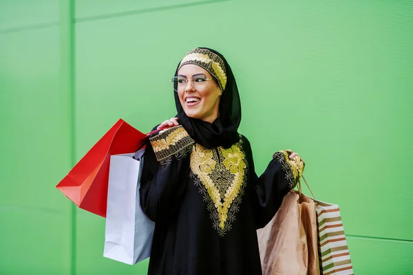 年轻迷人的哈哈大笑的女人穿着传统的衣服 手拿着购物袋走在户外 她对购物很满意 — 图库照片