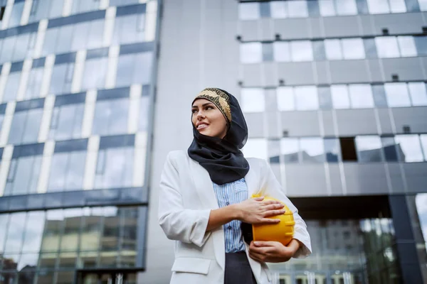 脇の下ヘルメットで彼女の会社の前に立って豪華な成功した笑顔肯定的な女性イスラム教徒の建築家の低角度ビュー — ストック写真