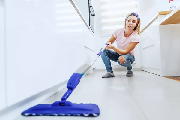 Attractive Worthy Caucasian Blond Young Housewife Crouching Cleaning Kitchen Floor — Stock Photo, Image
