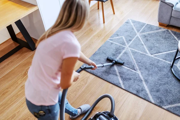 用真空吸尘器清洁客厅里的地毯的吸引人的有价值的高加索年轻家庭主妇的背景图 — 图库照片