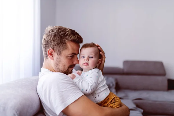 ソファの上のリビングルームに座っている間 彼の愛情6ヶ月の息子を胸の上に保持ハンサムな若い白人の父親 赤ん坊は目を背けている 無条件の愛の概念 — ストック写真