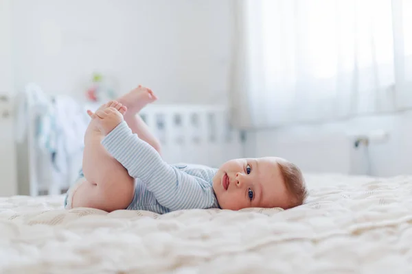 サイドビューの可愛いですCaucasian 6ヶ月若いです男の子服を着ています彼の足を保持し カメラを見ながらベッドルームに横たわって — ストック写真