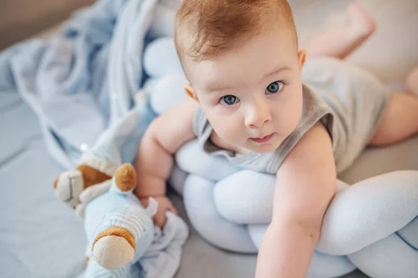 可愛いですCaucasian赤ちゃん男の子とともに大きな青い目あります胃の上にベッドルームでベッドの上に横たわっていると面白いですカメラ — ストック写真