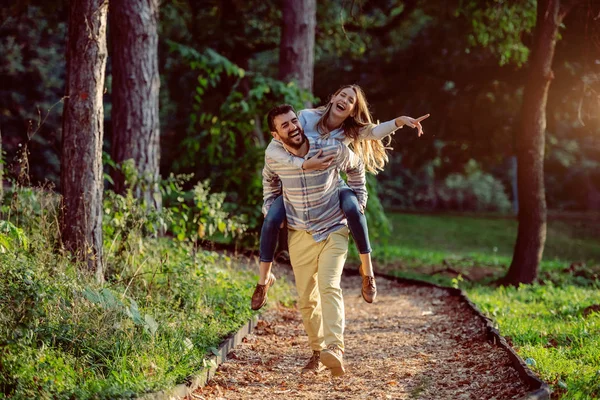 森の中を歩いている間にピギーバックを持つ遊び心のある幸せなハンサムな白人のカップル 自然の概念の冒険 — ストック写真